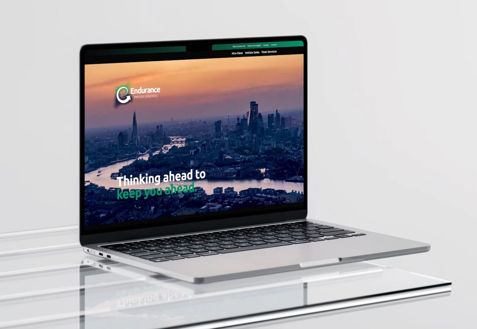 An open MacBook sits on a contemporary glass desk. On the screen is displayed the Endurance Vehicle Solutions website homepage.