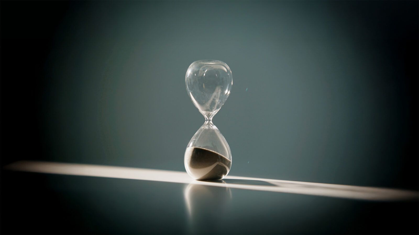 Closeup hand turning hourglass starting new countdown in sunlight. Sand flowing