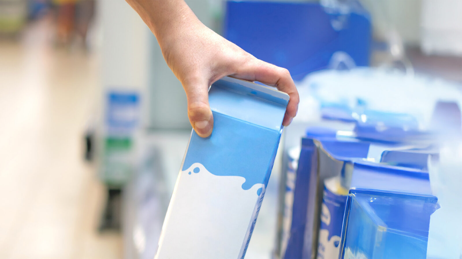 Hand taking a milk carton from supermarket shelf ready for consumption