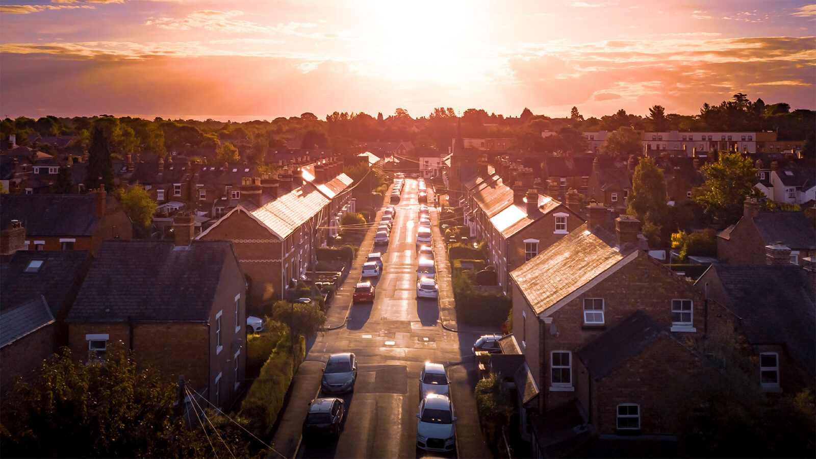 Sun setting with atmospheric effect over traditional British houses and tree lined streets. Dramatic, warm lighting creates a homely mood
